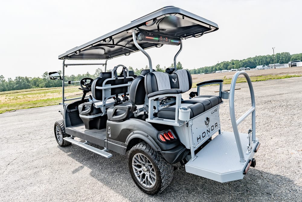 Four-seat luxury golf cart with a canopy, side steps, and a rear loading platform parked on a paved lot.