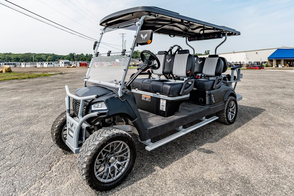 Four-row passenger golf cart with a roof and rugged tires, parked in a parking lot.