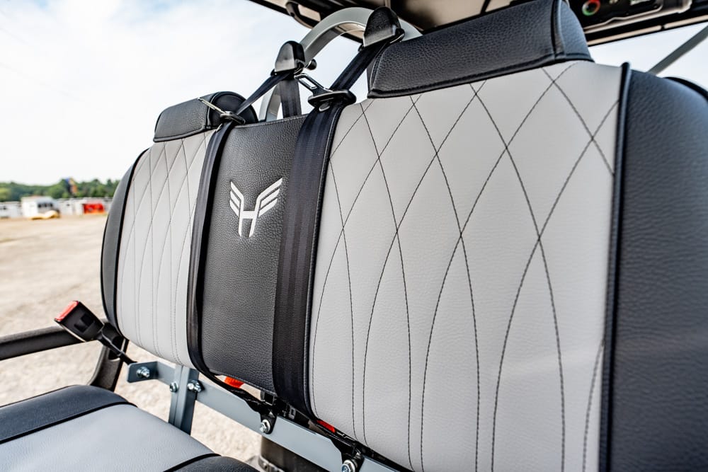 Close-up of gray, diamond-stitched airplane seats with a black center panel and a winged logo on the cushion (aircraft interior).