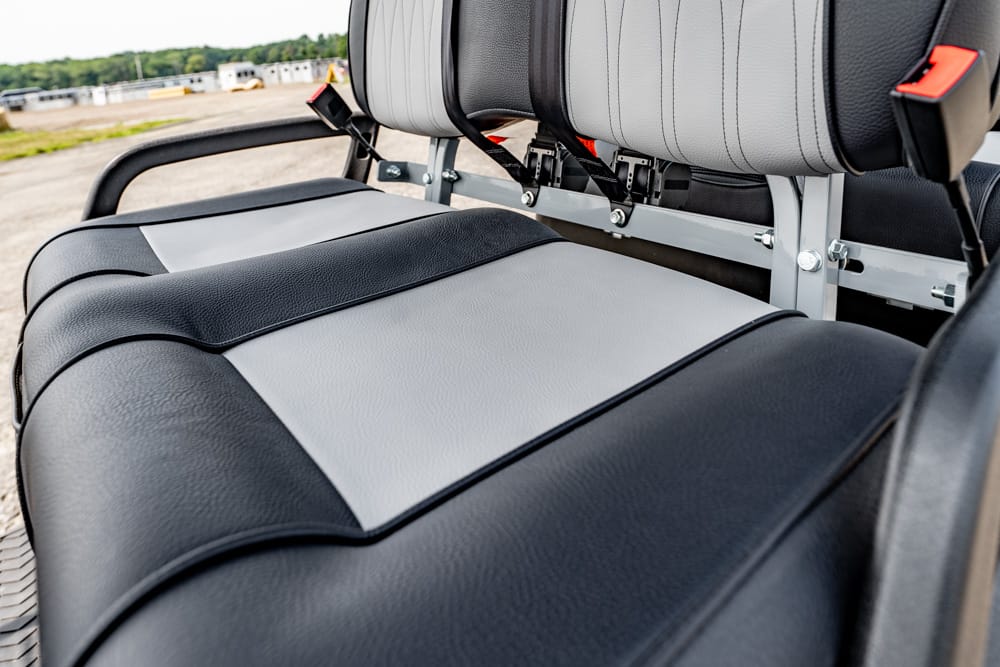 Close-up of black and gray leather car seats with seat belts and a metal frame in the background.