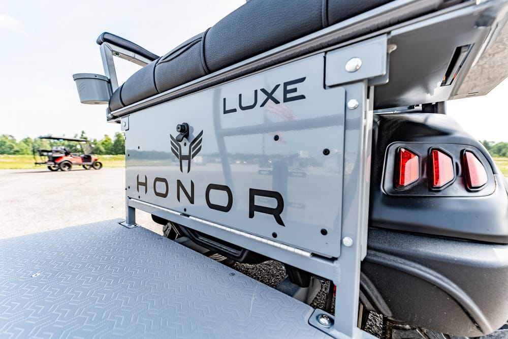 Rear side panel of a gray Luxe Honor golf cart with branding and red taillights on a diamond-plate platform