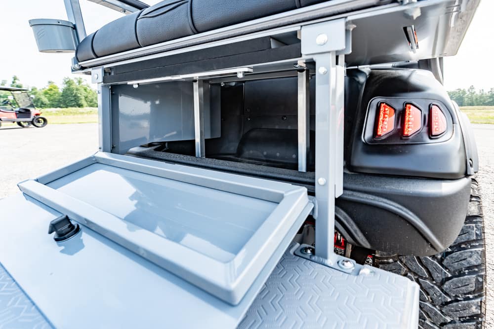 Open metal storage drawer beneath a cushioned seat on a rugged utility vehicle, showing the textured step and tire nearby.