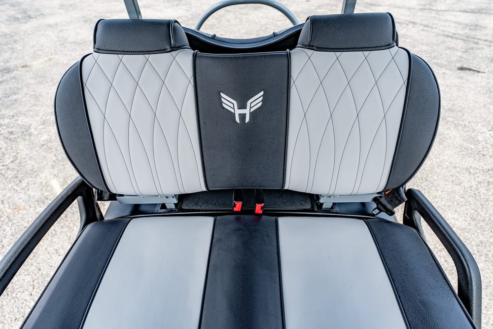 Close-up of a gray and black vehicle seat backrest with a quilted diamond pattern and a white winged emblem in the center