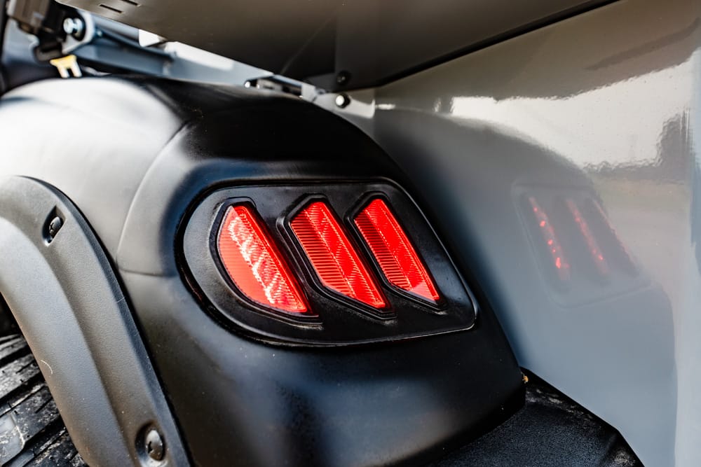 Close-up of three red LED taillights on a black motorcycle rear fender, with a gray body panel nearby.