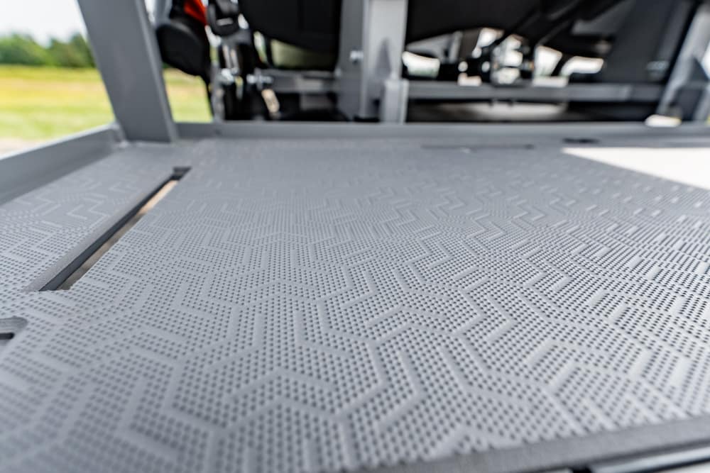 Close-up of a gray textured metal platform with a geometric non-slip pattern, part of a vehicle interior in the background.