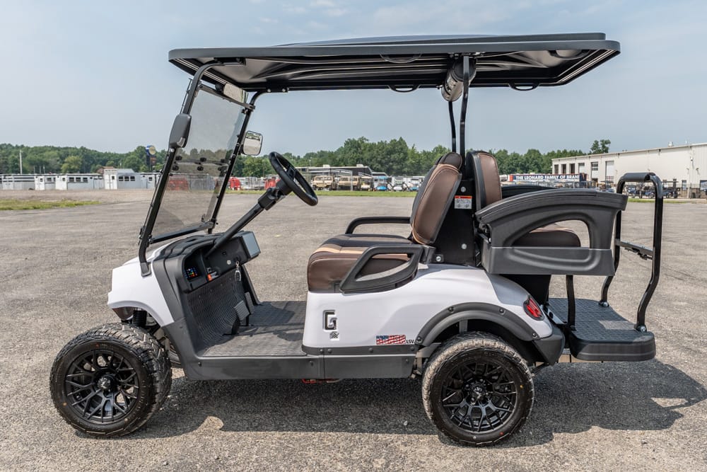 White golf cart with brown seats and a roof, parked on a gravel lot.