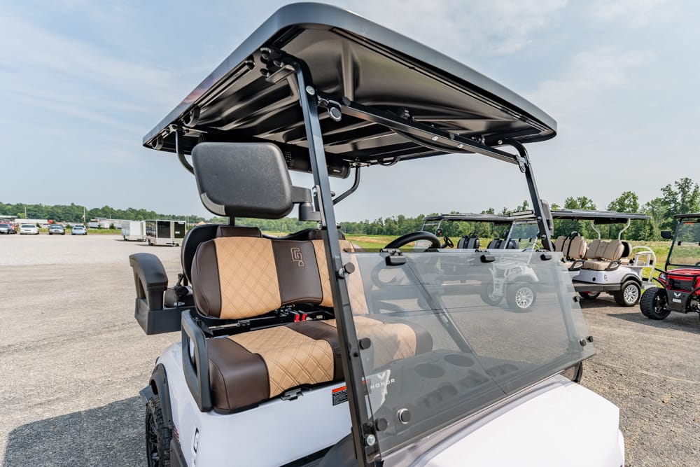 Golf cart with tan and brown quilted seats, open roof, and clear windshield in a parking lot.