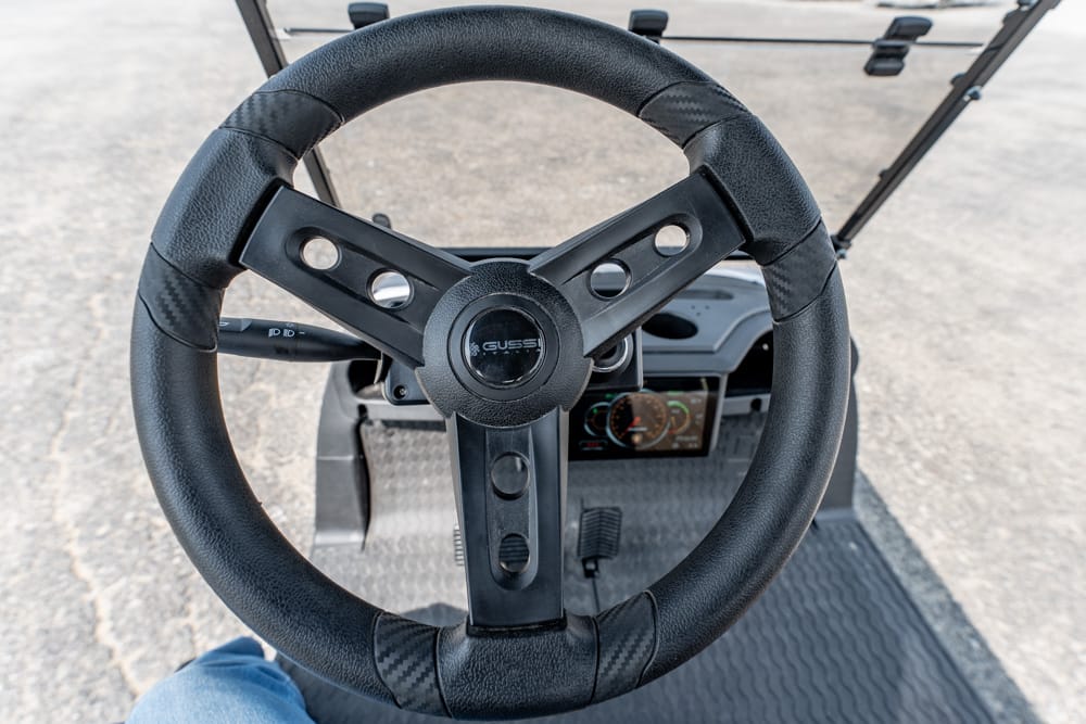 Steering wheel of a golf cart viewed from the driver's seat with the dashboard instruments in the background