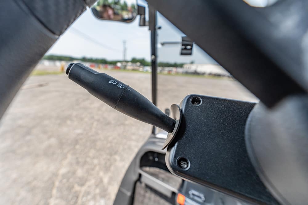 Vehicle headlight control stalk mounted on the steering column, shown within the car interior near the driver's seat.
