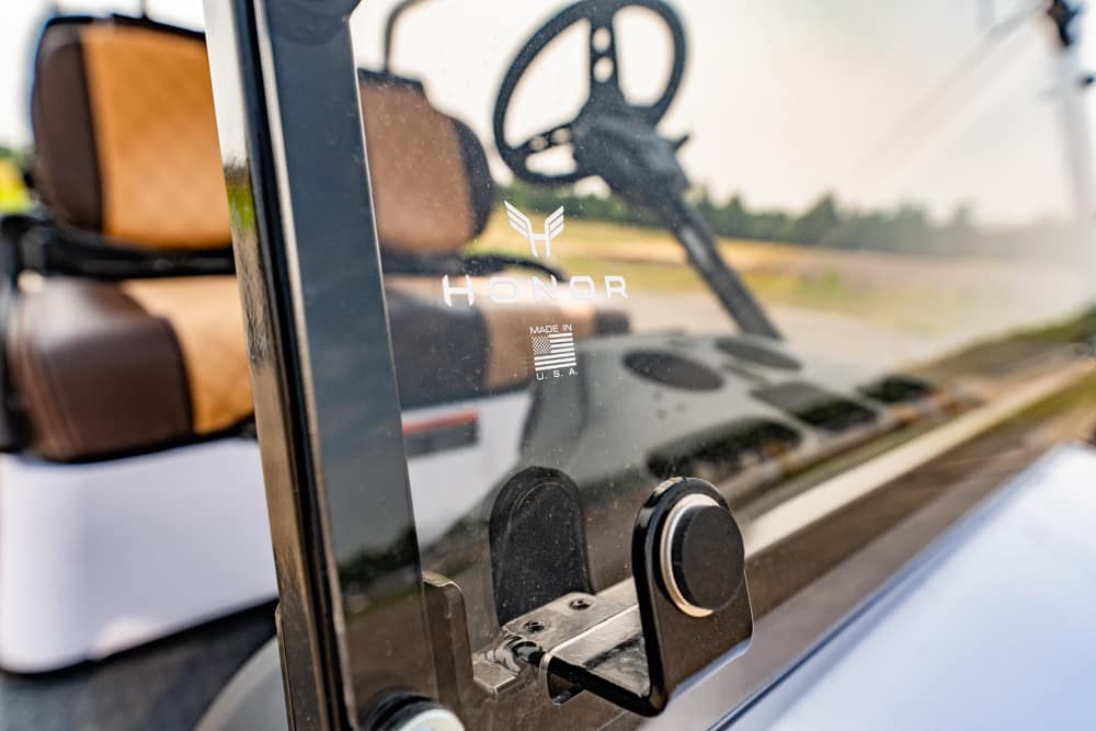 Close-up of a glass panel with the HONOR logo and 'Made in USA' text, with a golf-cart interior visible behind.