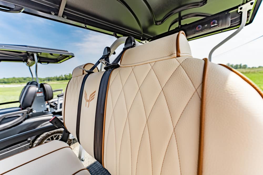 Beige quilted leather car seat inside an open-top vehicle, with a green field in the background.