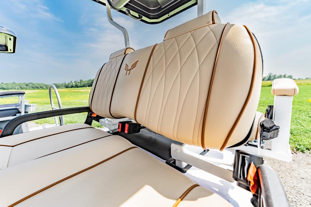 Close-up of beige leather golf cart seat with embroidered logo, outdoors on a sunny course.