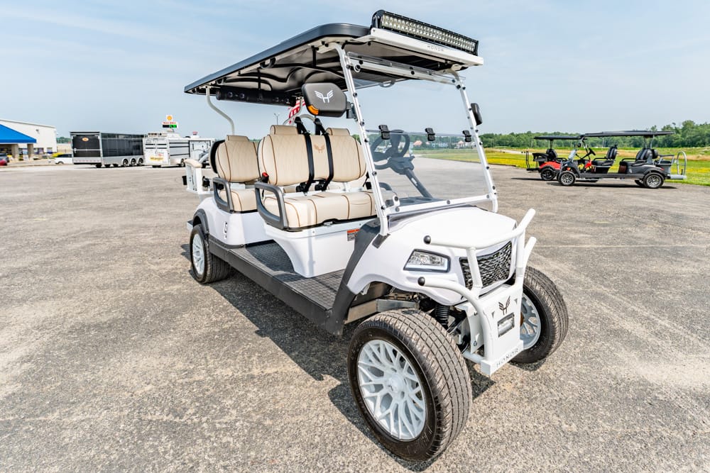 White four-seat golf cart with beige upholstery and a roof-mounted LED light bar on a paved lot.