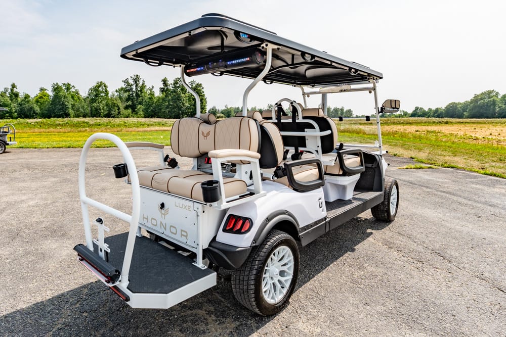 White luxury golf cart with beige upholstered seats and a large rear loading platform, parked on a paved lot.