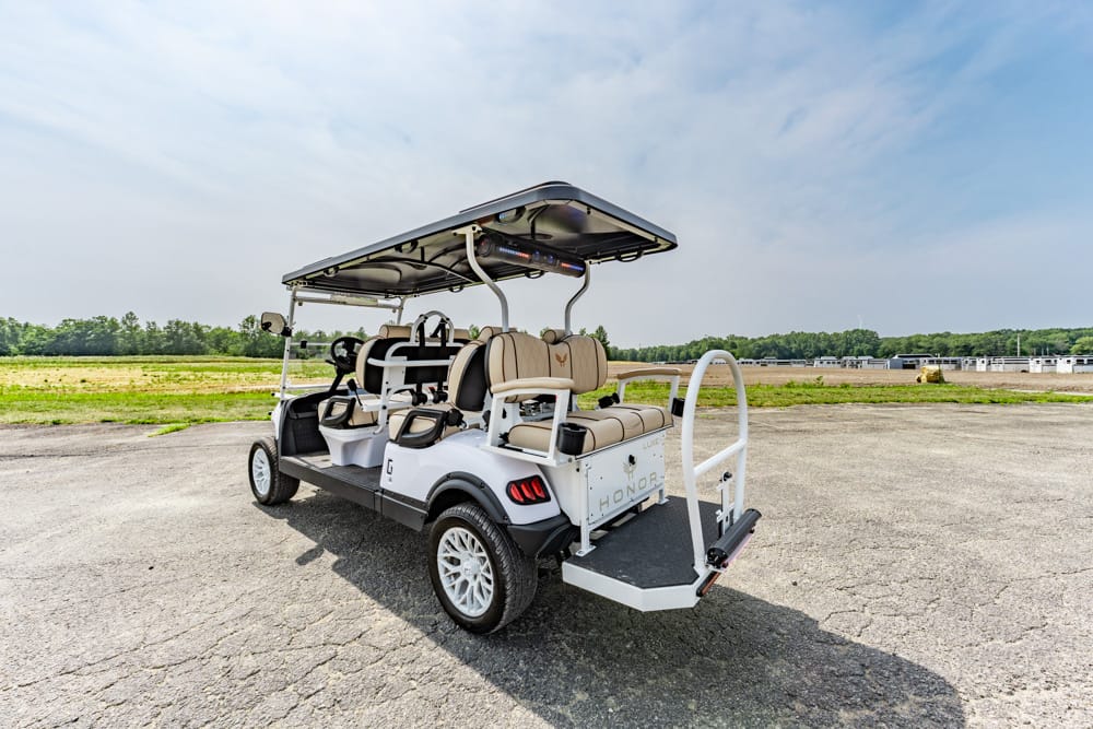 White six-seat golf cart with beige seats and a large canopy parked on a cracked asphalt lot.