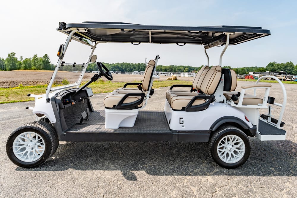 White six-seat golf cart with beige seats and a canopy, parked on a paved lot