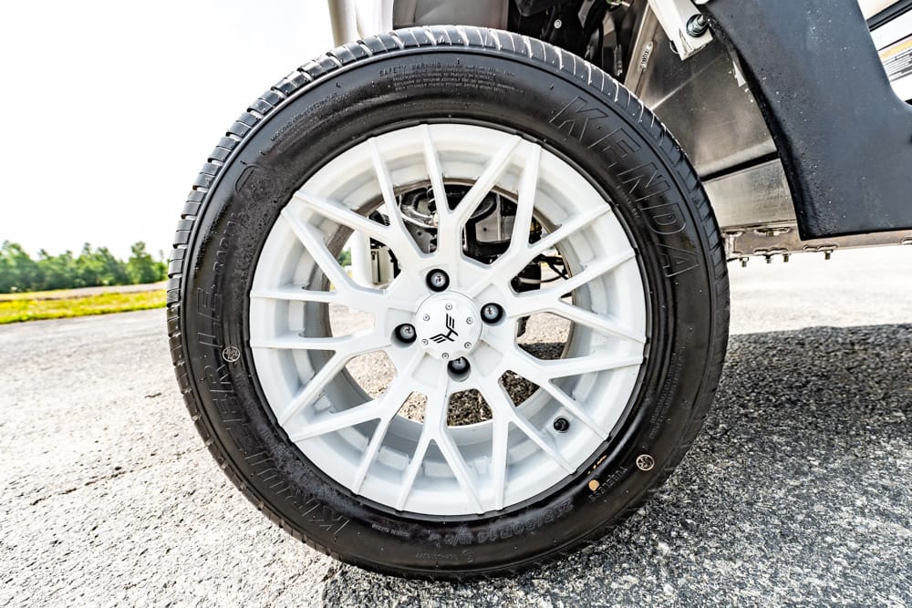 Close-up of a white multi-spoke car wheel with a black tire on an asphalt surface outside the vehicle.