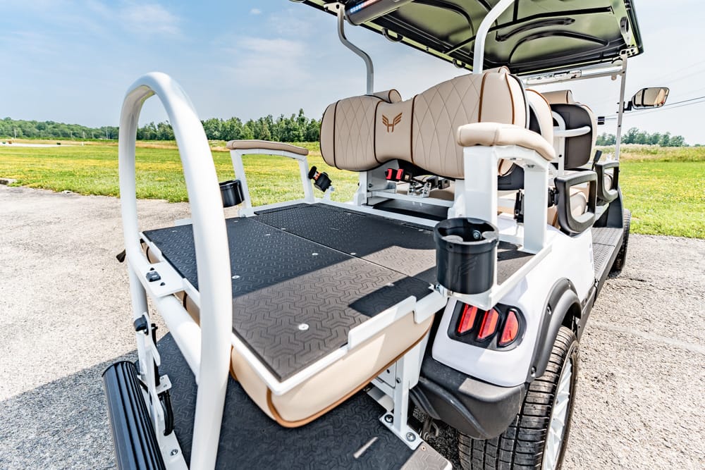 Rear view of a white luxury golf cart with tan quilted seats, diamond-plate rear deck, and cup holders on a sunny course.