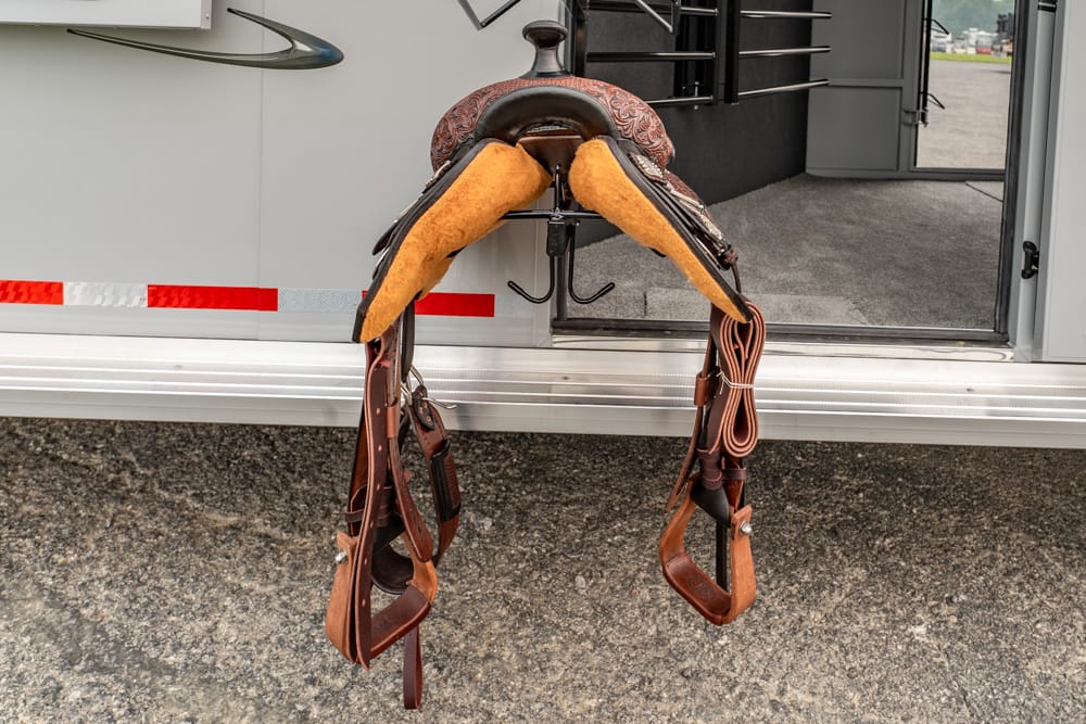 Leather horse saddle with stirrups hanging from the step of a trailer doorway.