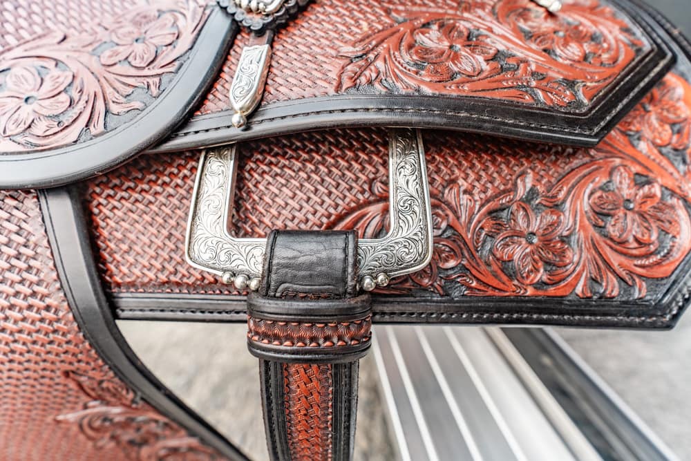 Close-up of a red and black tooled leather saddlebag with floral patterns and a silver engraved buckle.