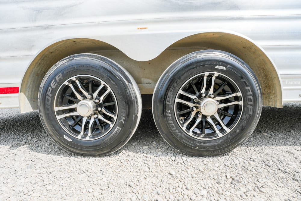 Dual-axle trailer with two black alloy wheels and Cooper tires, parked on gravel under the fender.