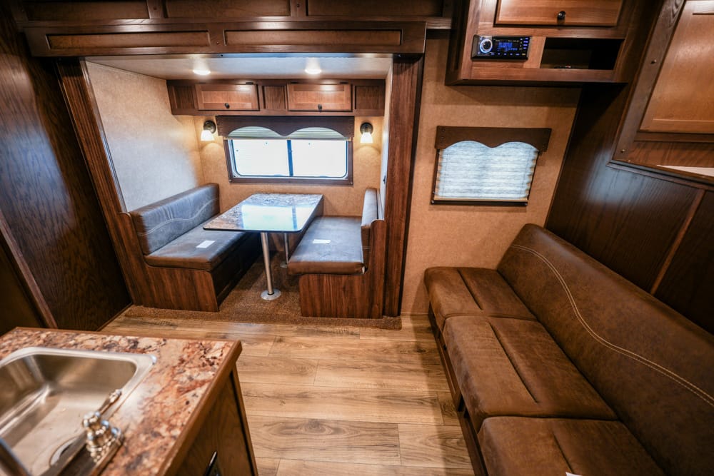 RV dining nook with a booth-style dinette around a rectangular table, beige walls, and wood cabinets overhead with a window nearby