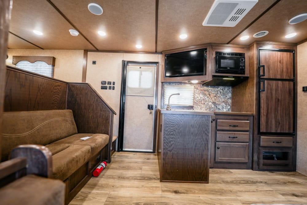 Interior of a compact RV with a brown sofa, wood paneling, and a kitchenette featuring a sink, countertop, and overhead microwave
