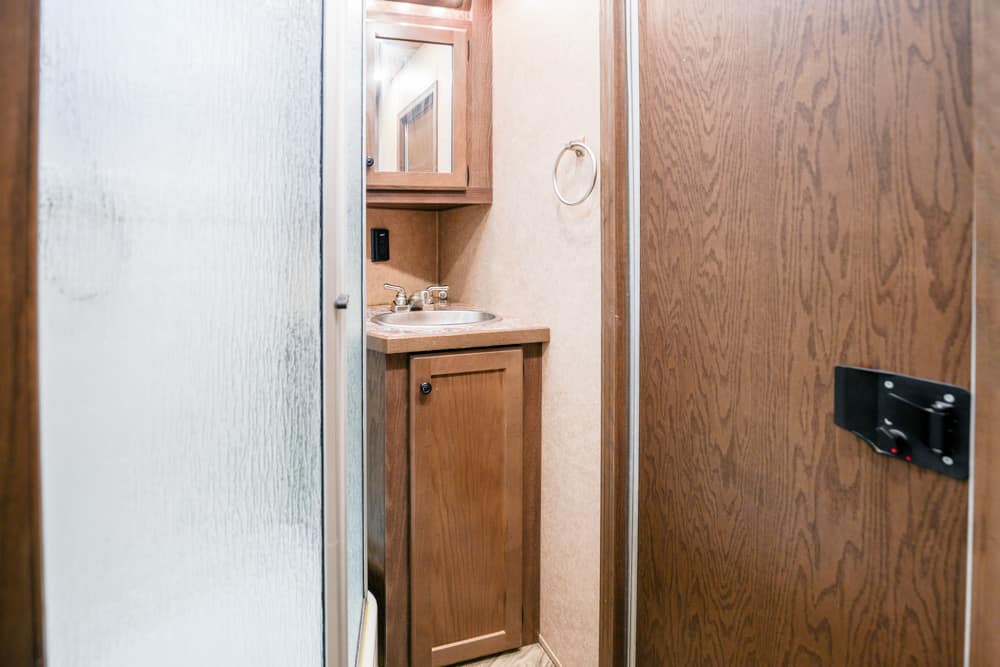Narrow RV bathroom with wooden vanity, round sink, mirror, towel ring, and frosted shower door.