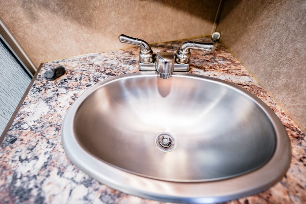 Stainless steel round sink with a two-handle chrome faucet on a speckled granite counter.