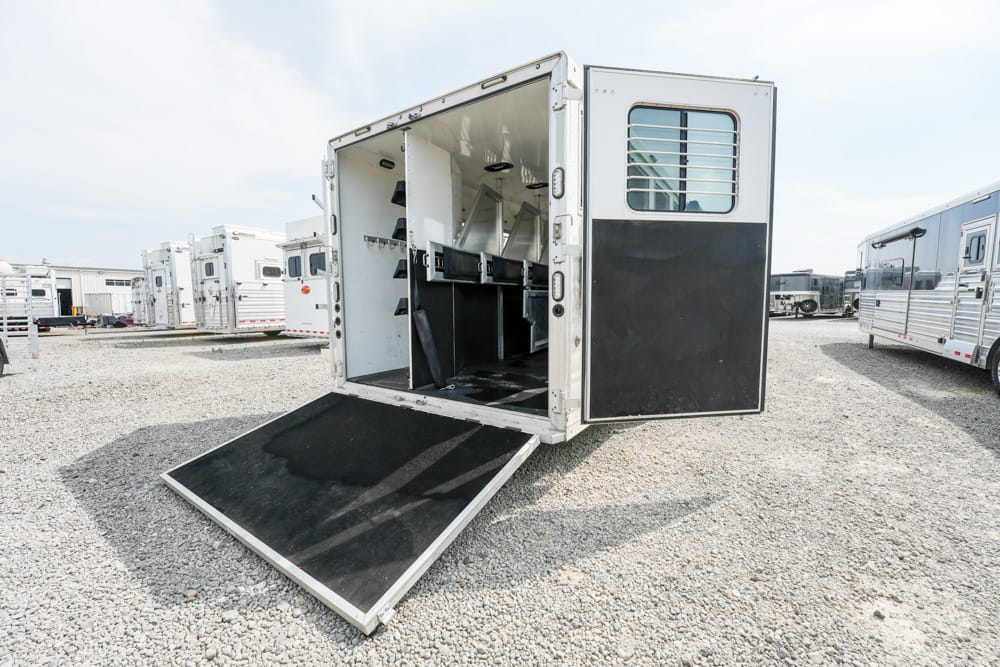 Open horse trailer with a lowered ramp in a gravel lot, other trailers visible in the background in a trailer yard.