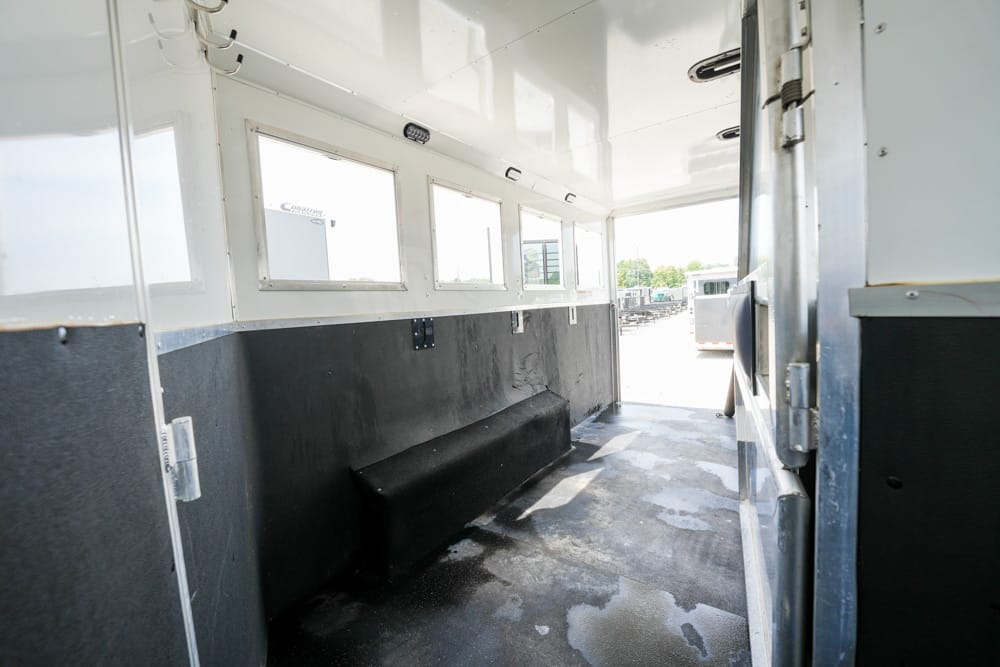 Empty trailer interior with a black bench along the wall, white upper walls, and daylight coming through windows.