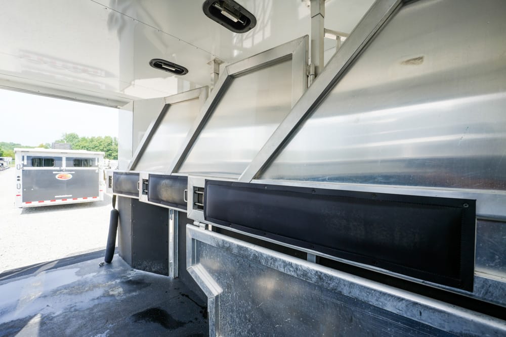 Industrial loading dock with metal ramps and a black protective panel along the trailer wall; a nearby trailer is visible outside under bright daylight