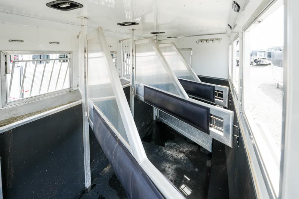 Interior of an empty livestock trailer with angled partitions and blue padded walls separating stalls inside a white metal trailer