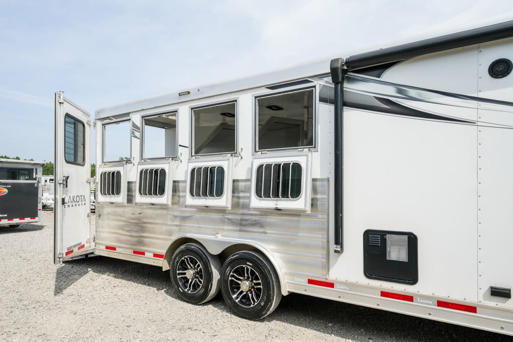 White horse trailer with multiple stall windows and open rear door, parked on gravel.