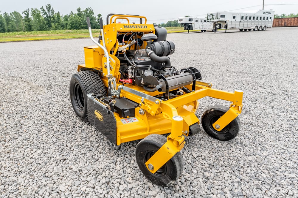 Yellow Hustler compact engine-powered roller on a gravel lot, with trailers in the distance.