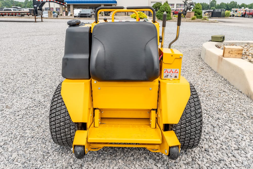 Rear view of a yellow ride-on industrial forklift on a gravel lot, with a large black seat and control levers behind it.