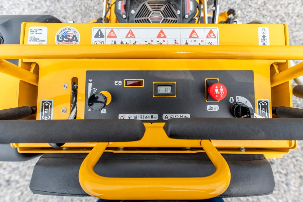 Yellow industrial machine cockpit with control panel, red emergency stop, digital readout, and safety labels.