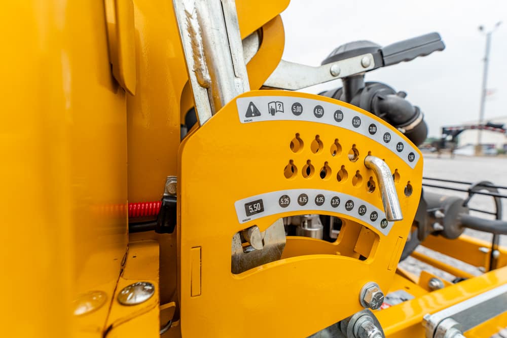 Close-up of a yellow construction machine's control panel with numbered adjustment settings and a locking handle.