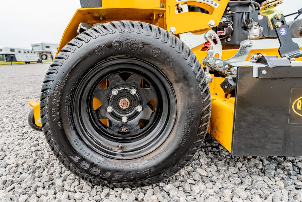 Close-up of a heavy equipment tire mounted on a black rim on a yellow construction vehicle, parked on gravel.
