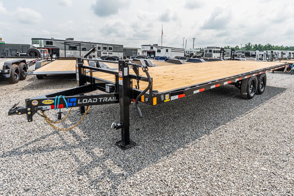 Load Trail flatbed trailer with a wooden deck in a gravel lot, surrounded by other trailers in a dealership yard.