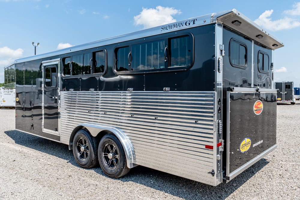Silver and black Showman GT horse trailer with ribbed aluminum lower panel, parked on gravel.