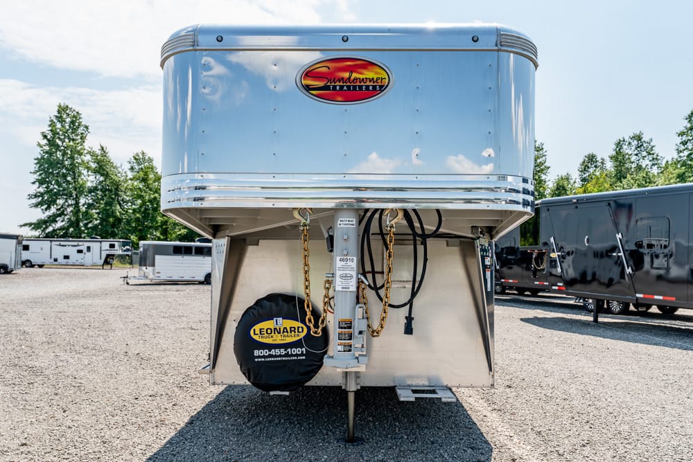 Front view of a shiny chrome Sundowner gooseneck trailer in a gravel lot, with a Leonard Truck & Trailer spare tire cover visible at the bottom left of the front