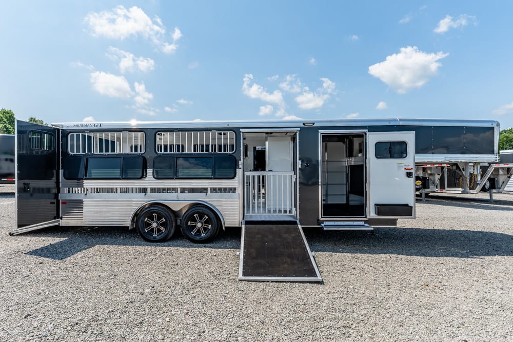 Silver gooseneck horse trailer with living quarters, side ramp down and open door, parked on gravel under a blue sky