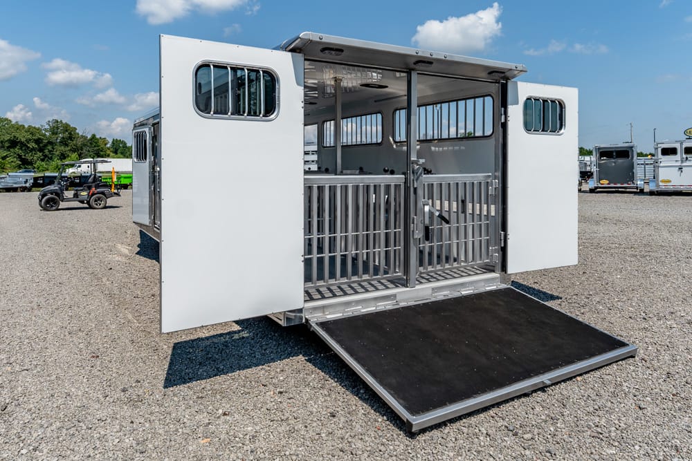 White horse trailer with open ramp, showing interior stalls and metal divider bars for horses.