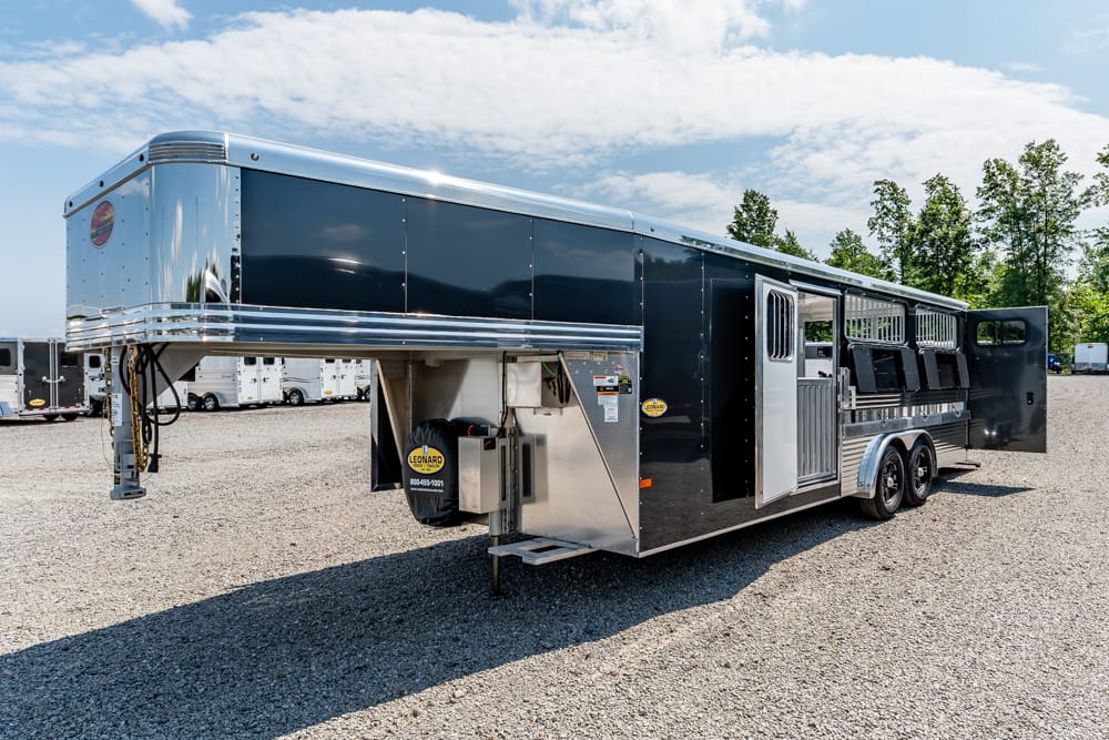 Black horse trailer with living quarters, gooseneck hitch, parked on a gravel lot with rear doors open.
