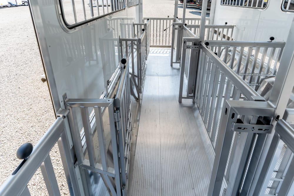 Interior of a silver livestock trailer with a grated metal ramp and multiple locking gates along a narrow walkway