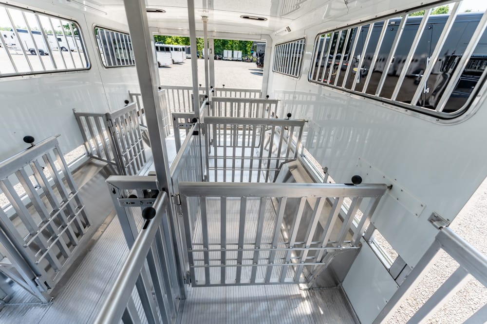 Interior of a metal livestock trailer with partitioned stalls and gates, empty at a parking lot.