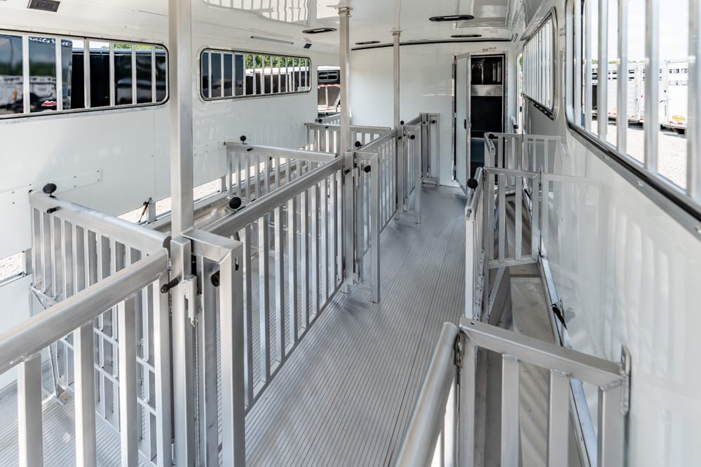 Interior of a white horse trailer with metal dividers and a narrow central aisle.