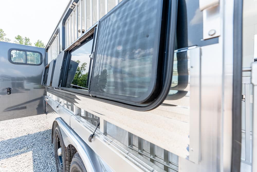 Exterior of a shiny aluminum trailer with large rectangular windows and an open side door, parked on a gravel surface.