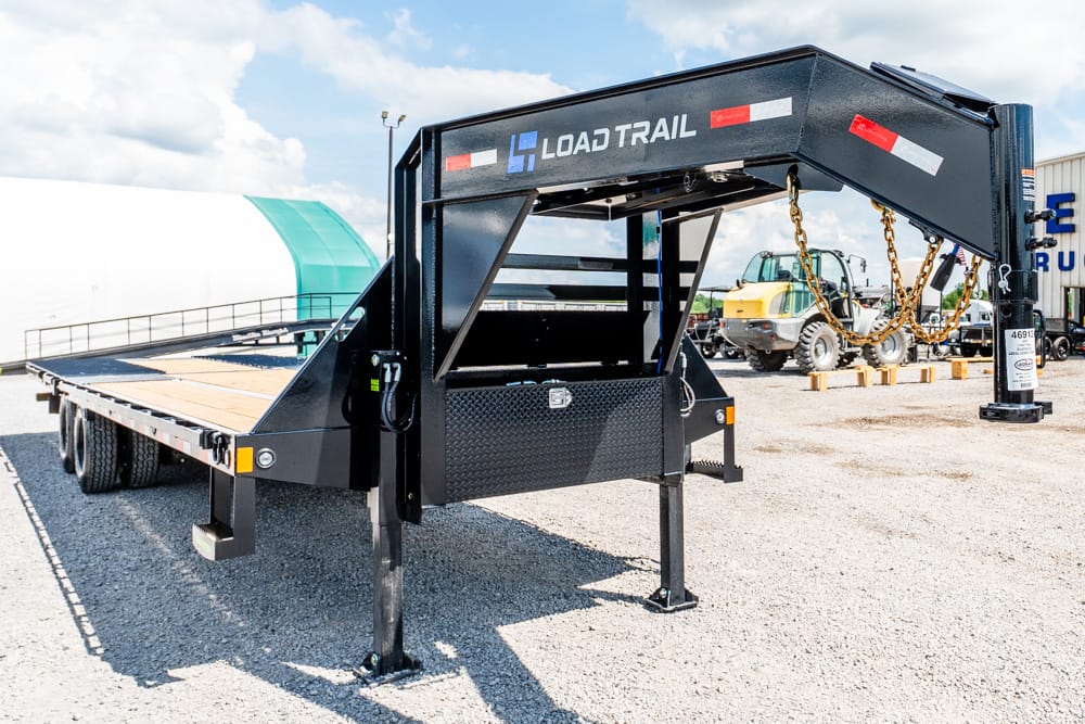 Black Load Trail gooseneck flatbed trailer with wooden deck in a gravel lot, ready for hauling equipment.